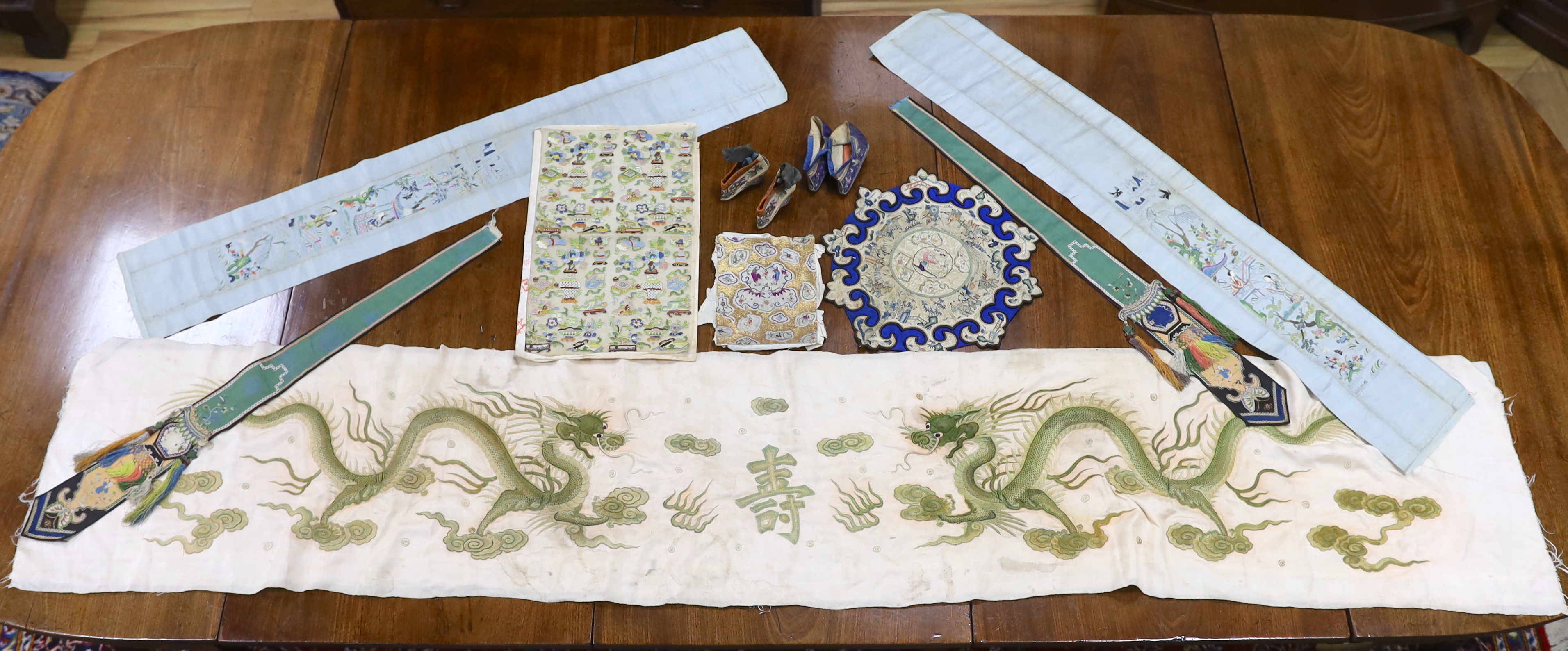 A collection of Chinese embroideries, to include a pair of tasselled embroidered panels to a wedding skirt, two pairs of Chinese children's shoes, a pair of embroidered sleeve bands, a panel of gauze of polychrome silk a